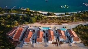 Vue aérienne d’un hôtel situé sur la côte, composé de plusieurs bâtiments, avec une piscine et des bateaux sur l’eau.