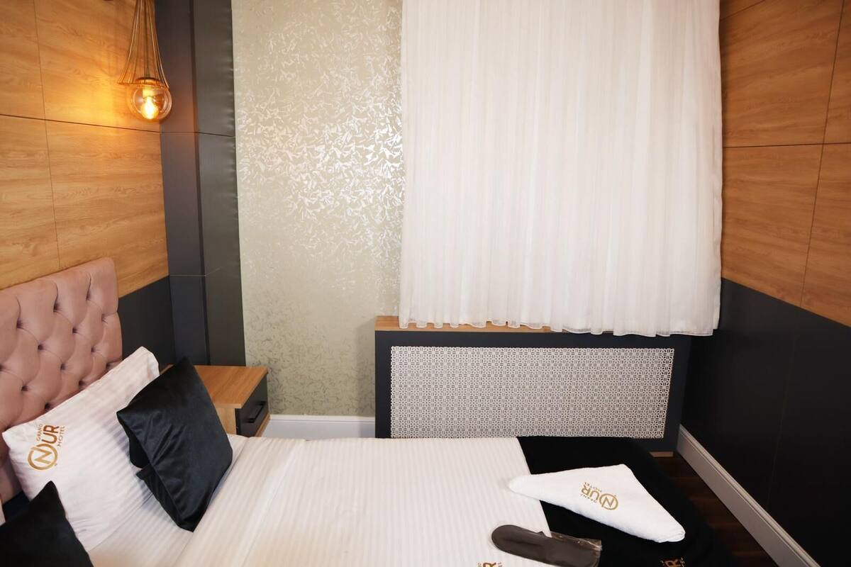 A modern hotel room with a tufted headboard, a patterned nightstand, and a neatly made bed with a white comforter and black pillows.