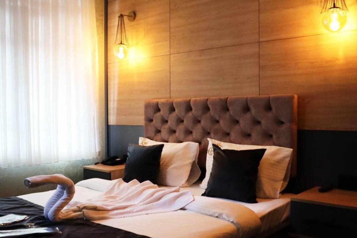 A modern hotel room with a large bed, wooden headboard, and two bedside lamps.
