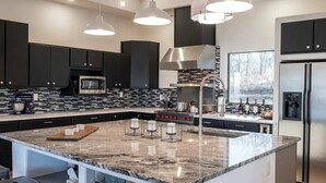 Una cocina moderna con una isla grande, armarios negros, electrodomésticos de acero inoxidable e iluminación colgante.