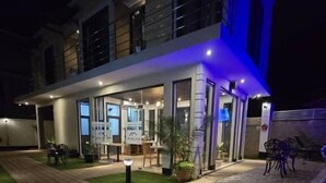 Un bâtiment moderne doté d’un toit plat, de grandes fenêtres et d’un espace extérieur aménagé avec une terrasse et des sièges.