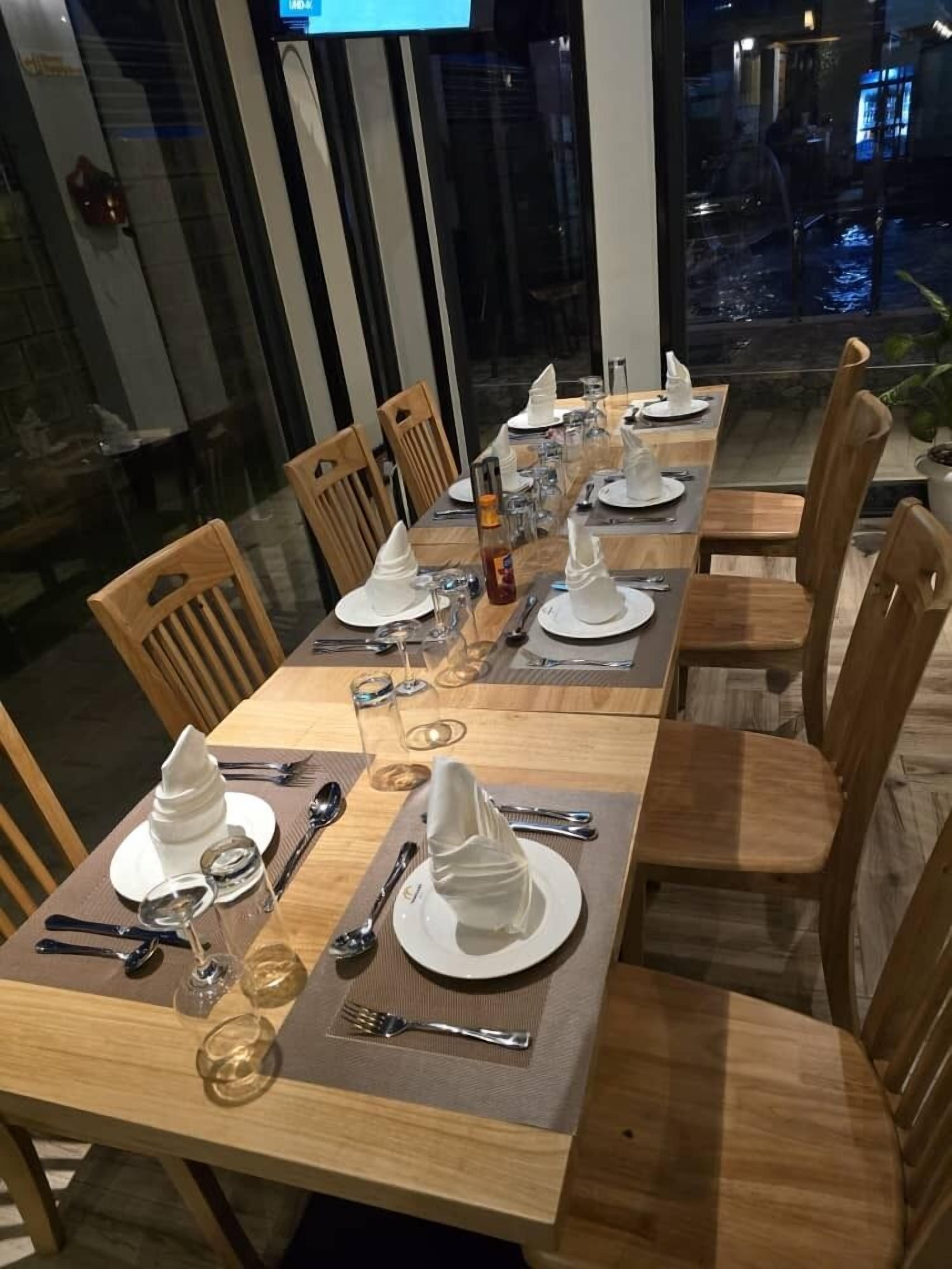 A dining area with wooden tables and chairs, set with white plates, glasses, and cutlery.