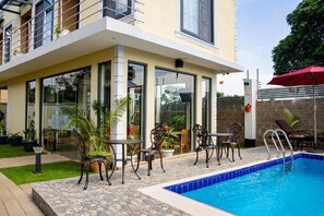 A modern building with a swimming pool, outdoor seating, and a well-maintained garden. - PRIMELAND HOTEL (Moshi)