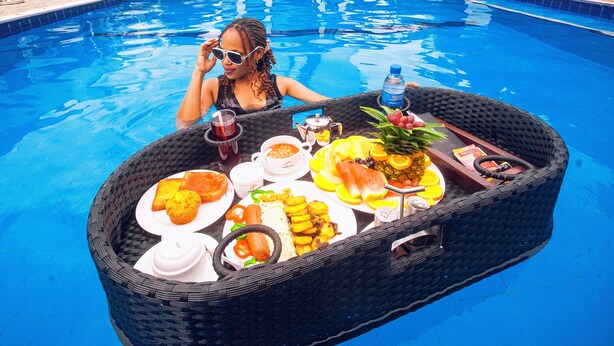 Un espace de restauration aménagé au bord de la piscine, avec une table, de la nourriture et un bâtiment d’hôtel en arrière-plan.