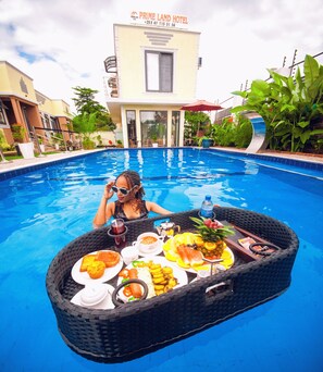 A poolside dining setup with a table, food, and a hotel building in the background. - PRIMELAND HOTEL (Moshi)