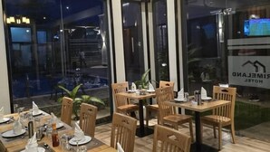 Un restaurant avec des tables et des chaises en bois, de grandes fenêtres et un plafond orné d’un lustre.