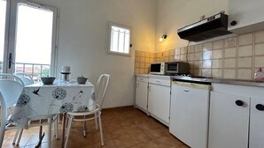 A compact kitchen with white cabinets, a tiled backsplash, a microwave, and a gas stove. There is a dining table with chairs and a window providing natural light.