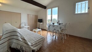 A room with a bed, a dining table with chairs, a TV, and a window with bars.