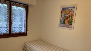 A small room with a single bed, a window with lace curtains, and a poster on the wall. - Charming 2-room apartment with balcony near the beach (Villers-sur-Mer)