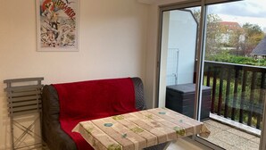 A balcony with a table covered in a protective cloth, a sofa with a red blanket, and a poster on the wall. - Charming 2-room apartment with balcony near the beach (Villers-sur-Mer)