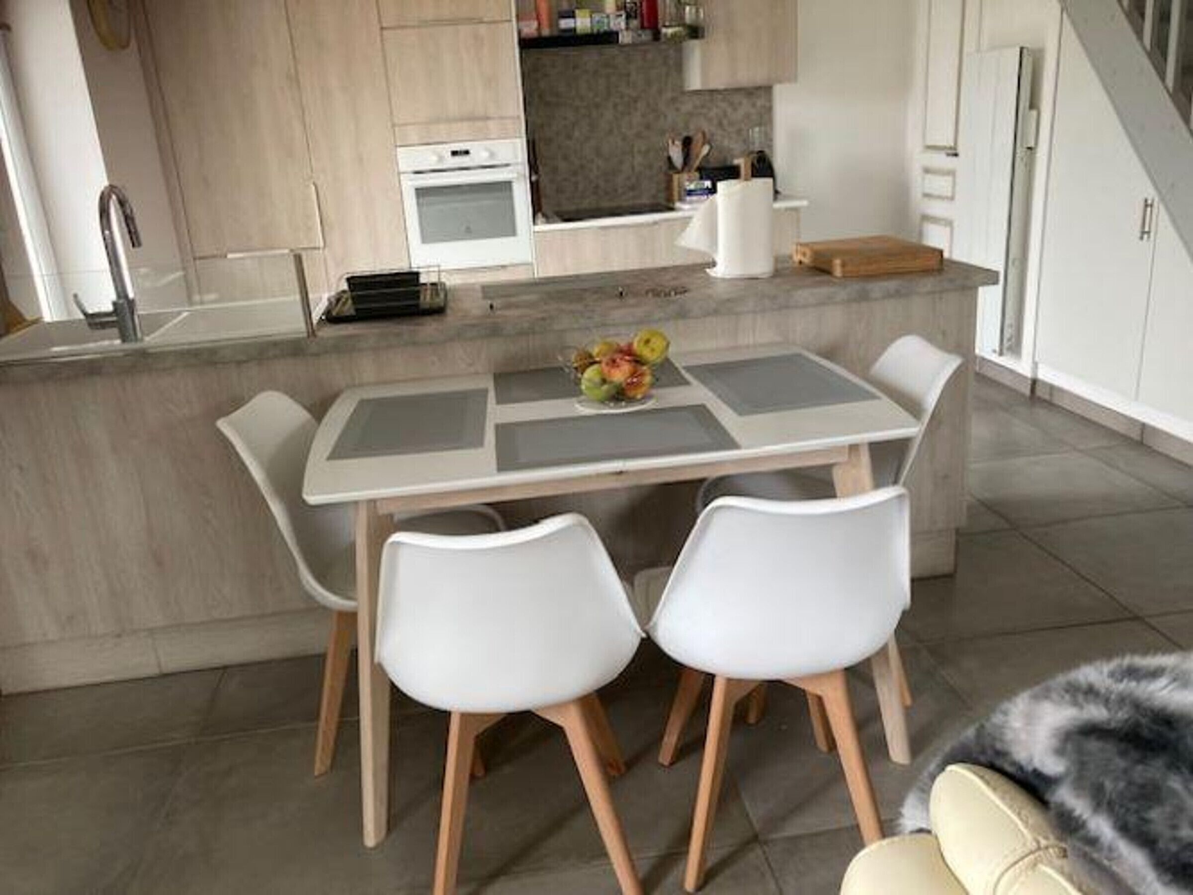 Uma cozinha moderna com ilha central, cadeiras brancas e uma mesa de jantar.