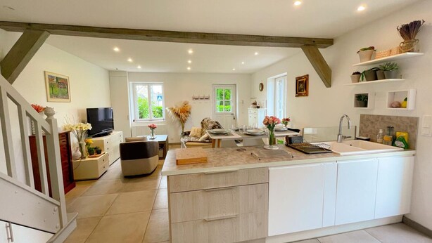 A spacious kitchen with a central island, a dining area with a sofa, and a TV in the living room. - Charming Cottage with Modern Amenities, Large Garden, and Terrace in Scenic Touraine (Saint-Aubin-le-Dépeint)