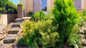 A building with a stone staircase leading to a door, surrounded by lush greenery and flowering plants. - Charming Cottage with Modern Amenities, Large Garden, and Terrace in Scenic Touraine (Saint-Aubin-le-Dépeint)
