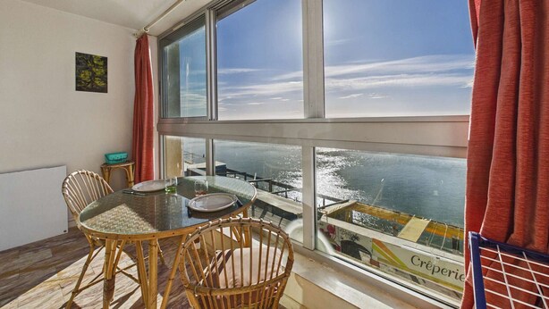 A room with a large window, wicker chairs, a round table, and a view of the sea. - 2-room apartment with terrace on beachfront for rent (Le Grau d'Agde)