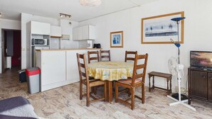A compact living space with a dining table, chairs, a kitchen area, and a television. - 2-room apartment with terrace on beachfront for rent (Le Grau d'Agde)