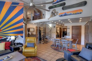 A spacious living area with a yellow armchair, a dining table with chairs, a staircase, and a kitchen area.