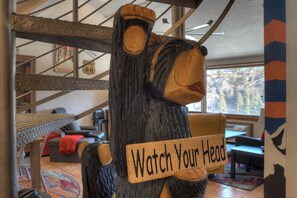 A wooden sculpture of a bear holding a sign that says "Watch Your Head".
