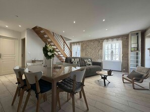 A modern living room with a dining area, a staircase, and a stone wall.