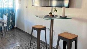 Quarto moderno com mesa de vidro, dois banquinhos de madeira, televisão de tela plana na parede e tapete estampado.
