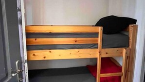 Uma cama box com dois níveis, uma porta à esquerda e um travesseiro vermelho na cama inferior.