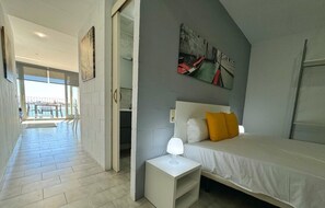 Un dormitorio con cama, mesita de noche, lámpara y un cuadro en la pared.