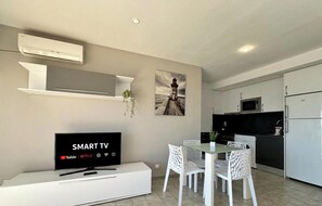 A modern kitchen with a built-in microwave, a white dining table with chairs, and a flat-screen TV displaying 'SMART TV' with streaming service logos.