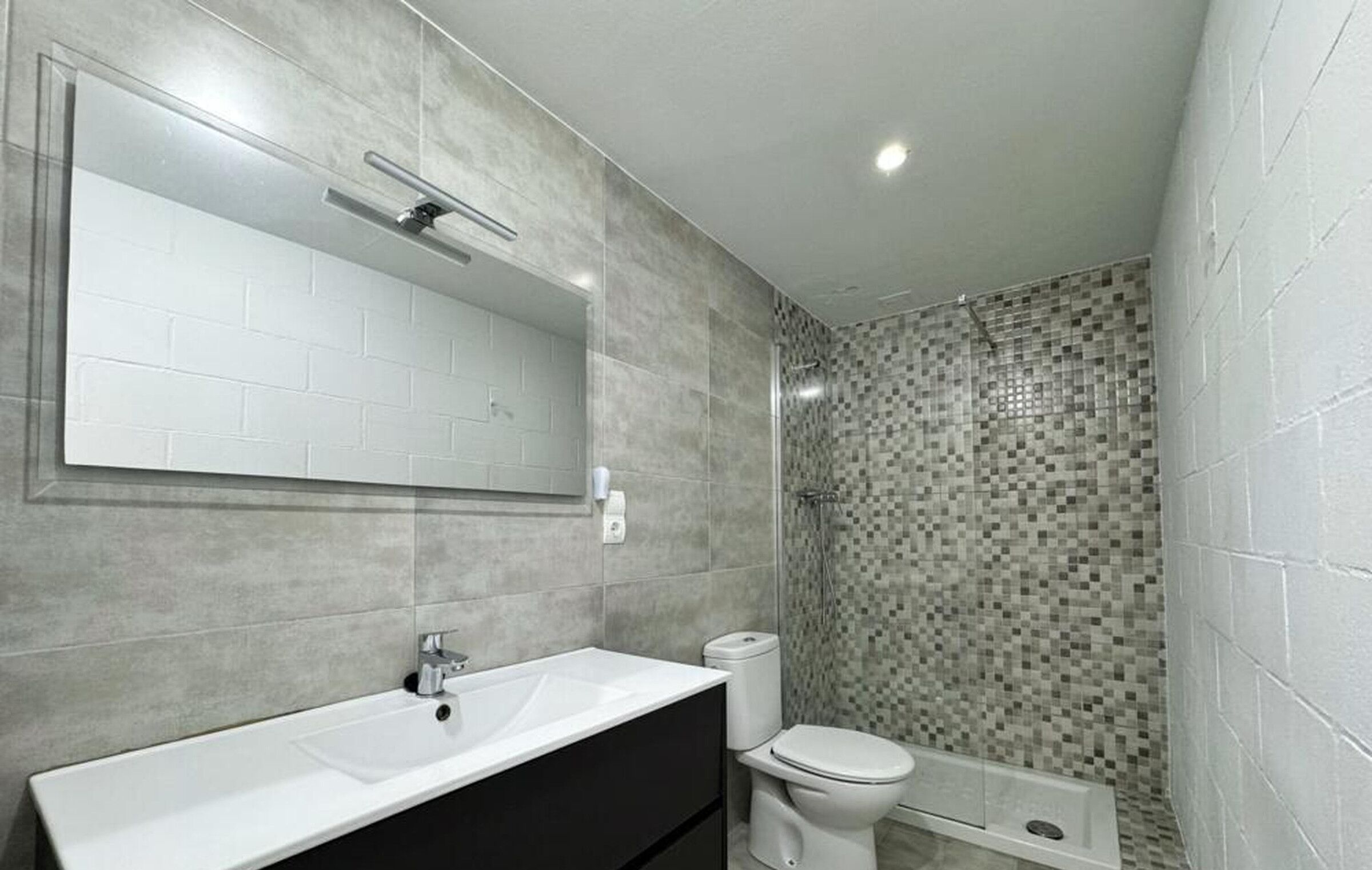 Un baño con un lavamanos blanco, un inodoro y una zona de ducha con mosaicos.