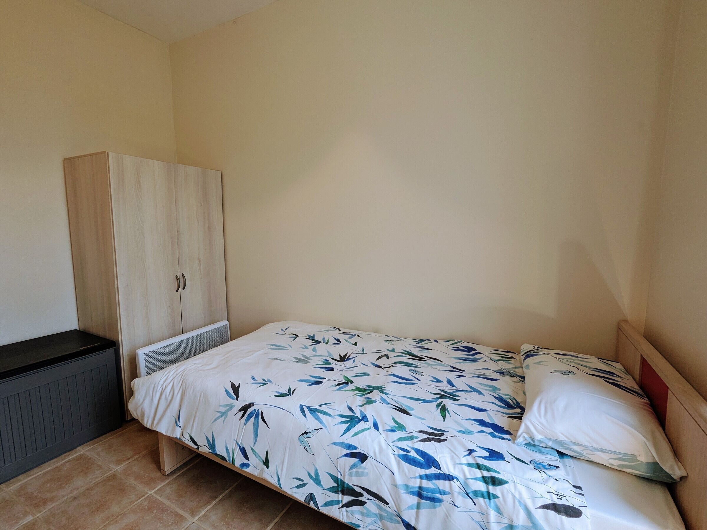 Ein kleiner, schlichter Raum mit einem Bett, einem Kleiderschrank und einer Heizung.