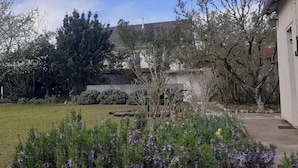 Um imóvel residencial com gramado bem cuidado, diversas plantas floridas e árvores já adultas.