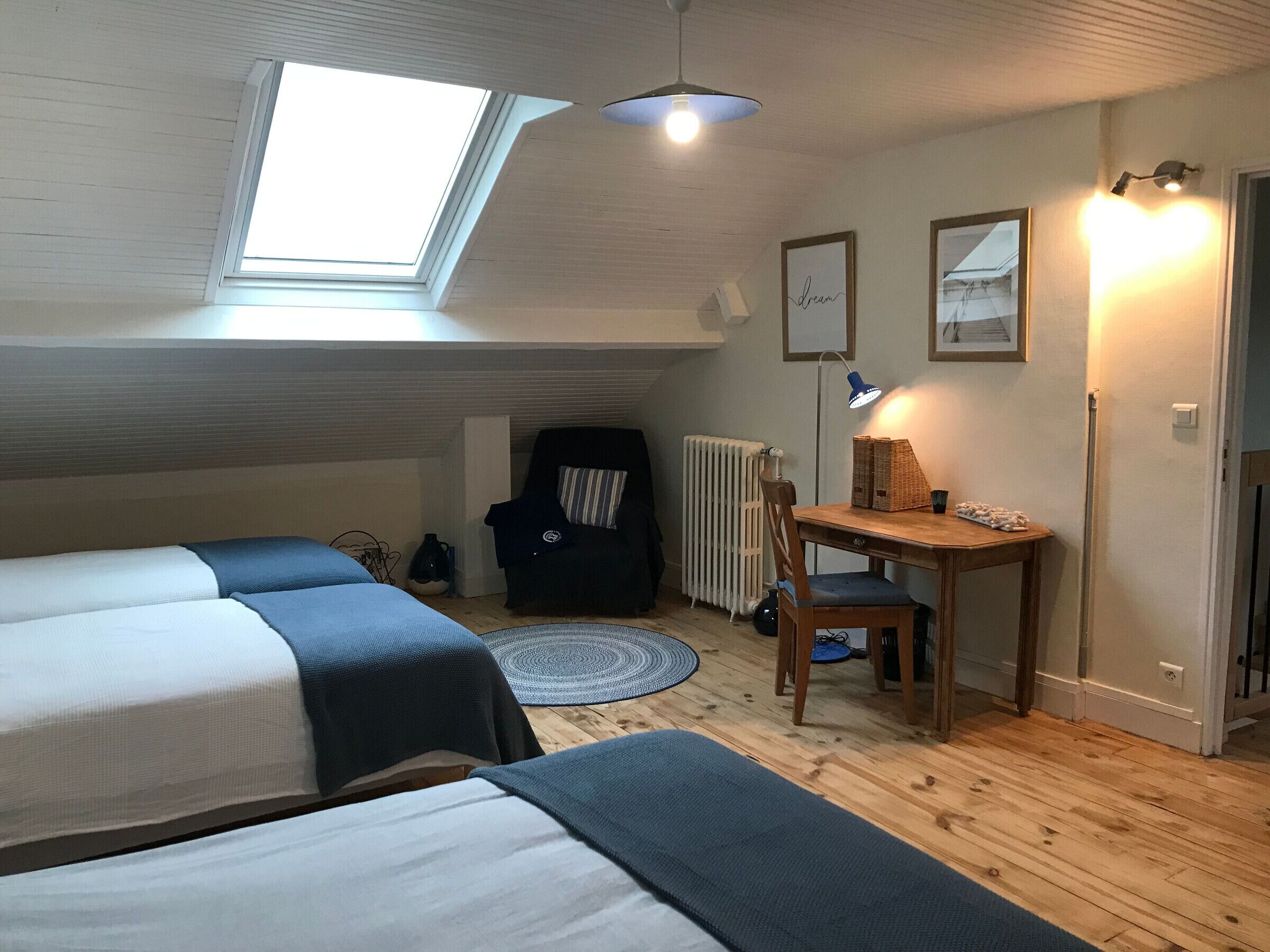 A cozy attic bedroom with a skylight, a desk with a lamp, a chair, and a radiator.