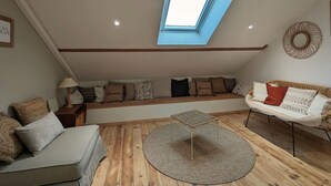 Een knus loft slaapkamer met een schuine kap, dakraam, een ingebouwde bank, een ronde salontafel en een bank.