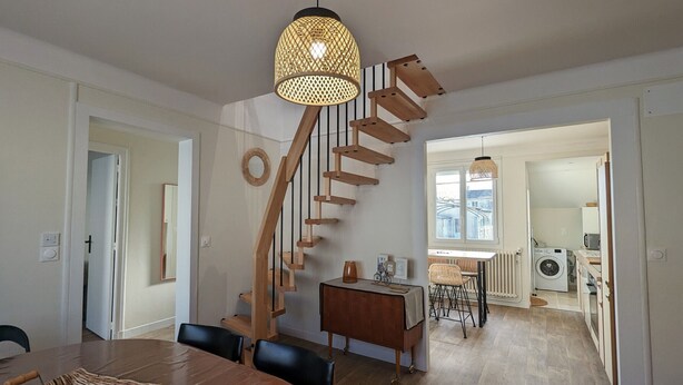 Een modern interieur met een houten trap, een eethoek met een ronde tafel, en een keuken die zichtbaar is door een open doorgang.