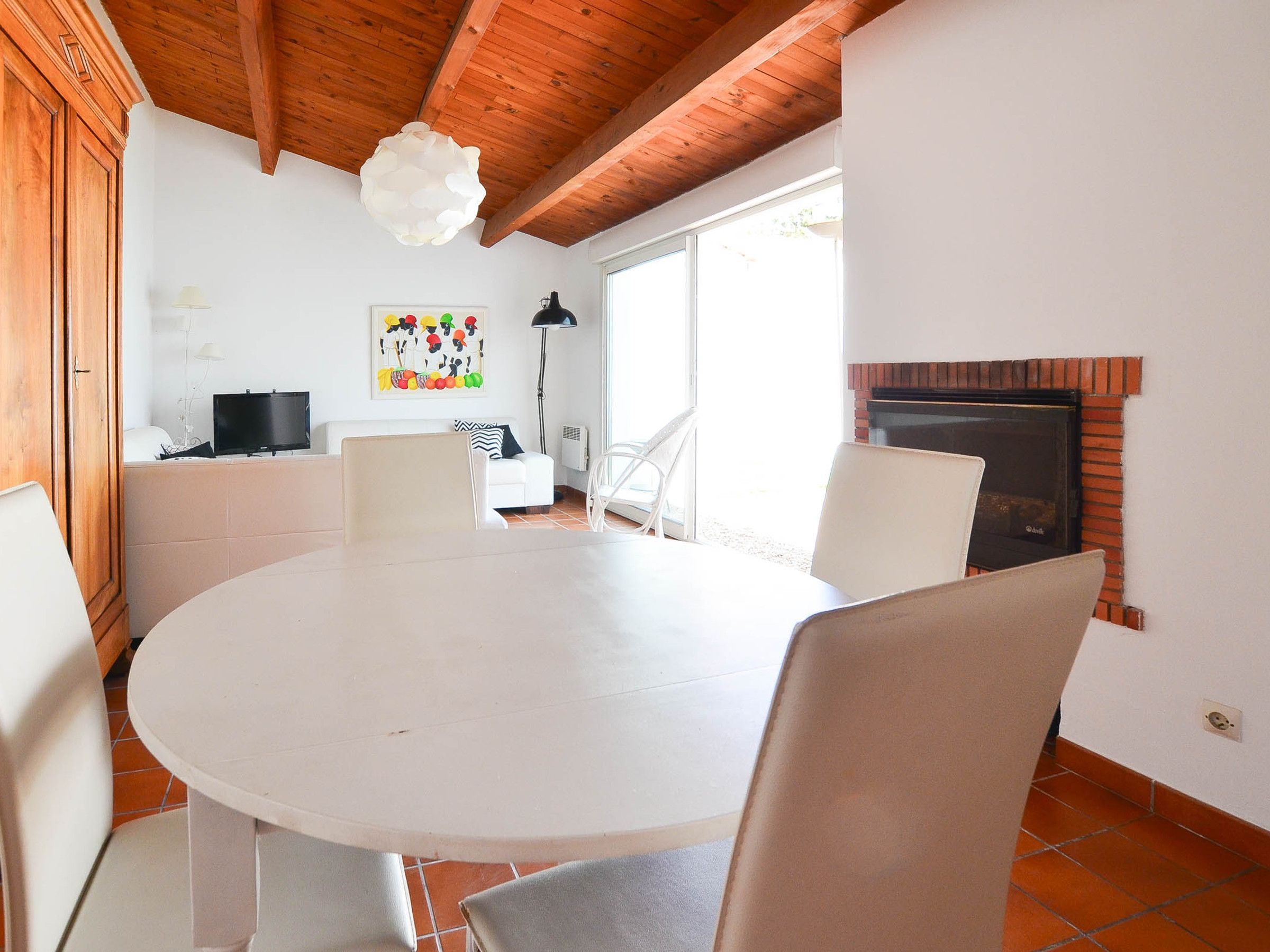 A dining area with a round table, chairs, a fireplace, and a kitchen in the background.