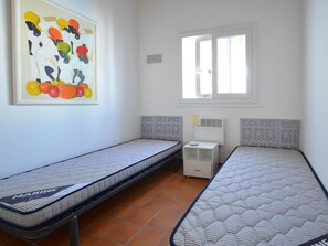 A room with two single beds, a window, a radiator, and a wall-mounted artwork.