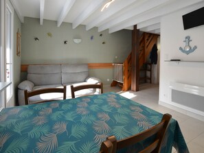 A room with a bed, a table with a patterned tablecloth, a sofa, and a staircase leading to another level.