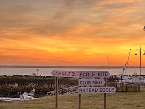 A signpost with directions to various nautical and sailing facilities, a rocky shoreline, and a calm body of water during sunset. - House with terrace, near beach and shops (La Palmyre)