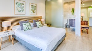 Une chambre à coucher moderne avec un grand lit, une tête de lit en bois et deux reproductions botaniques encadrées accrochées au mur.
