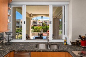 A kitchen with a granite countertop, a double sink, and a view of a balcony with outdoor furniture.