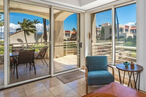 Una habitación moderna con una puerta corrediza de vidrio que da a un balcón, un sillón azul, una mesita redonda y una mesa de centro de madera.