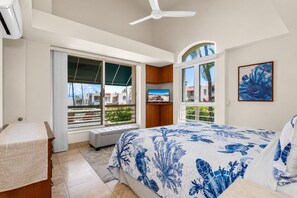 Une chambre avec un grand lit, une fenêtre donnant sur un beau paysage, un ventilateur de plafond et un tableau accroché au mur.