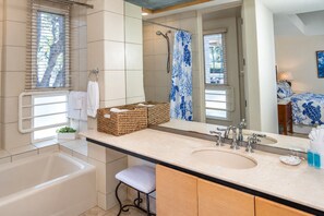 Baño con bañera, lavamanos, espejo, cestas de mimbre y cortina de ducha.