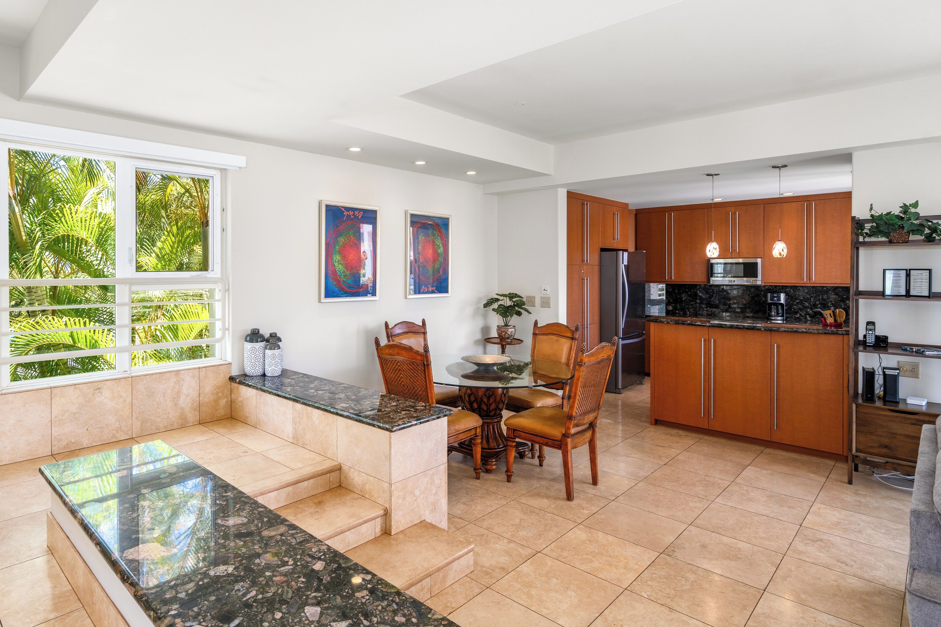 A modern kitchen with wooden cabinets, a granite countertop, and a dining area with a glass table and chairs.
