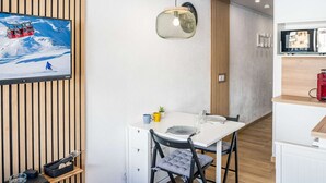 Una stanza moderna con una parete in listelli di legno, un tavolo bianco con due sedie, una piccola pianta e una sveglia.
