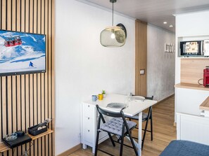 A modern room with a wooden slat wall, a white table with two chairs, a small plant, and a clock. - Renovated 18m² Apartment, Val Thorens - 2 people, balcony, near slopes (Val Thorens)