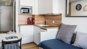 Una piccola cucina attrezzata con forno a microonde, macchina del caffè e lavello. È presente un tavolo con sedie e un letto con cuscini.