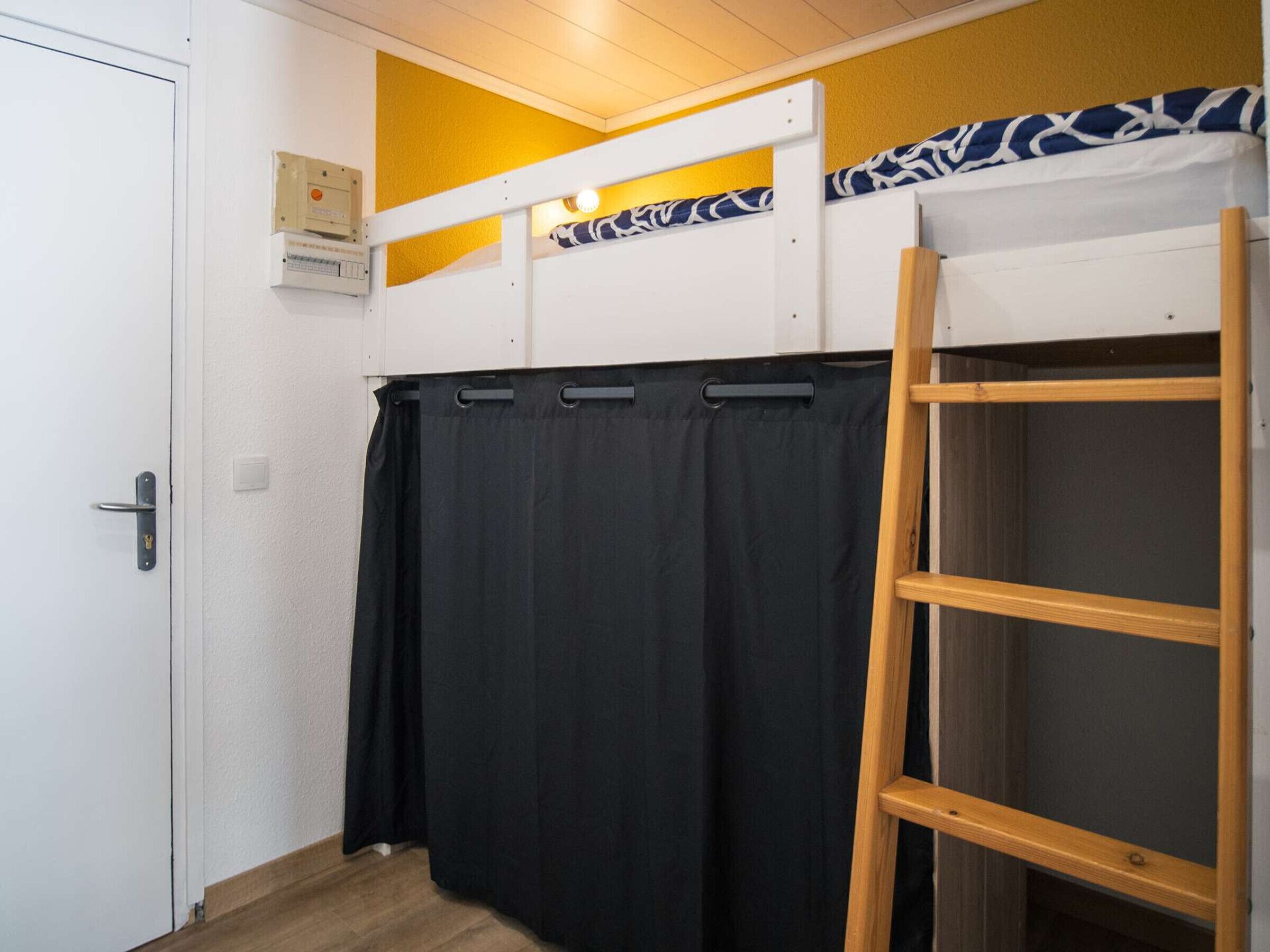 A room with a bunk bed, a black curtain, a wooden ladder, and a white door.