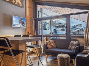 Una habitación acogedora con paredes de madera, un sofá, una mesa de comedor y un amplio ventanal con vistas a una montaña nevada.