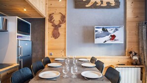 Un comedor con una mesa de madera dispuesta para seis personas, rodeada de sillas. En la pared, una decoración de cabeza de venado y un cuadro con una imagen de un esquiador.