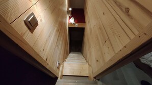 Una escalera de madera que lleva a una habitación con una pared de acento roja y una pequeña mesa con una lámpara.