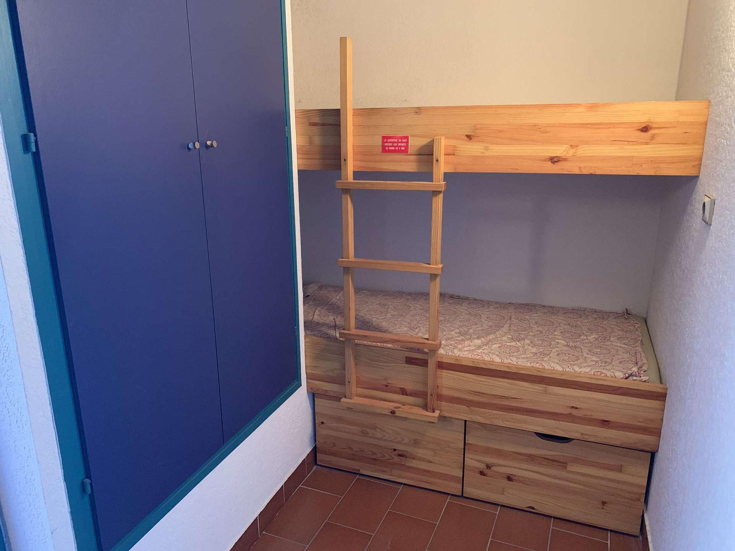 Una cama litera con escalera, un armario azul y un pequeño mueble de madera.